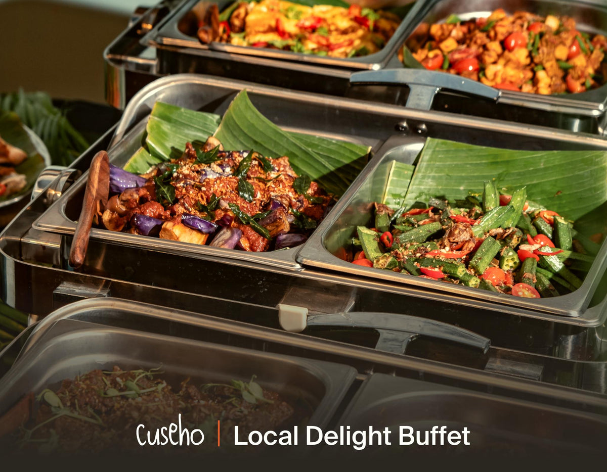 A buffet display of local dishes in stainless steel chafing trays lined with banana leaves, featuring colorful cooked vegetables and proteins. The text 'Cuseho | Local Delight Buffet' is visible at the bottom.
